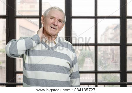 Senior Caucasian Man Having Neck Pain. Old Sick Male With Neckache In Windows Background.