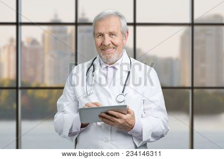 Senior Doctor Using His Tablet Computer At Work. Physician Using Tablet Computer In Hospital Lobby, 