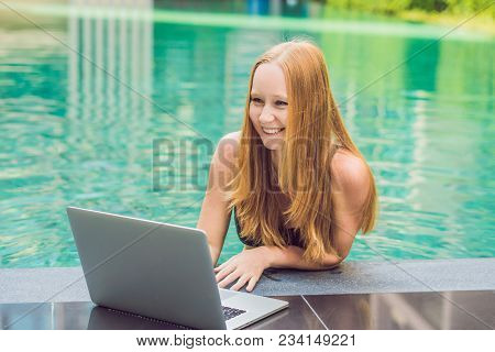 Young Female Freelancer Sitting Near The Pool With Her Laptop In The Hotel Browsing In Her Smartphon
