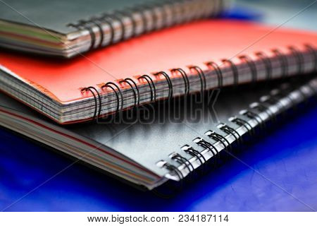 Three Closed Spiral Notebooks In A Pile On Blue Background.
