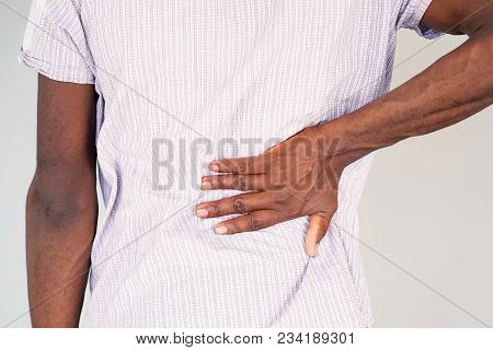 Close-up View Of A Young Man With Pain In Kidneys On Gray Background. Young Man With Back Ache Clasp