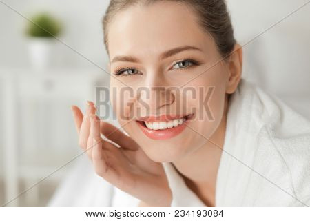 Young woman applying cream onto her skin, closeup