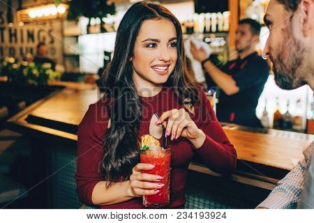 Amazing Girl Is Sitting At The Barman's Stand And Holding A Glass Of Cocktail In Her Hands. She Is S