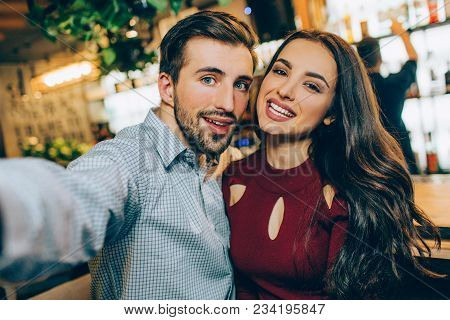 Selfie Of Two Beautiful People Sitting Together In A Bar. He Is Taking A Picture Of Them While She I