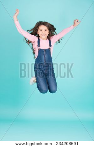 Happy Child In Jeans Overall Jump, Fashion. Small Girl With Long Brunette Hair Jump, Energy. Fashion
