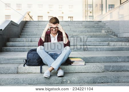 Desparate Student Sitting On The Stairs Working On Laptop Outdoors In The University Campus. Man Rai