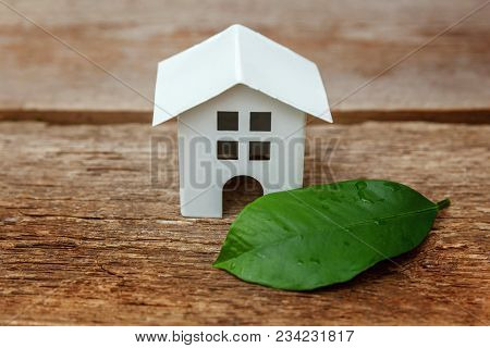 Miniature White Toy Model House With Green Leaves On Wooden Backgdrop. Eco Village, Abstract Environ