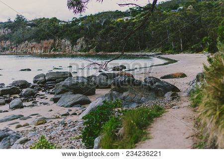 Deserted Beach In Hobart, Tasmania With Rocks And Walkpath In The Foreground On An Overcast Day With