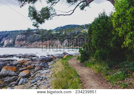 Deserted Beach In Hobart, Tasmania With Rocks And Walkpath In The Foreground On An Overcast Day With