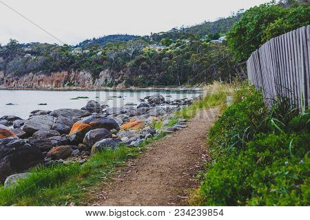 Deserted Beach In Hobart, Tasmania With Rocks And Walkpath In The Foreground On An Overcast Day With