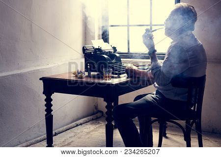 Elderly man sitting smoking pipe with retro typwriter on wooden table