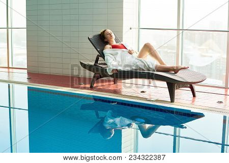 Full Length Portrait Of Beautiful Young Woman Relaxing Lying In Wicker Lounge Chair By Swimming Pool