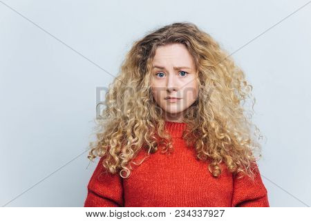 Photo Of Displeased Unhappy Young Woman With Curly Bushy Blonde Hair, Frowns Face In Bewilderment, W