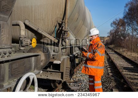 A Railway Worker In High Visibility Clothing Inspecting A Railroad Wagon During A Scheduled Maintena