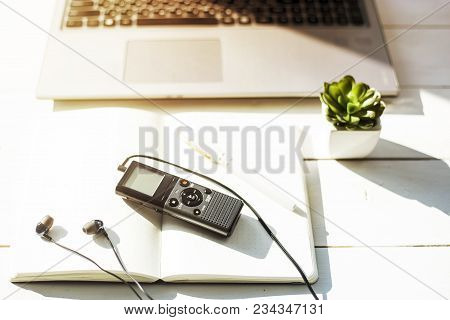 Dictaphone With Headphones On A Light Worktable Of A Journalist With A Notebook, A Green Succulent A