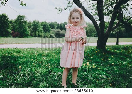 Little Girl In A Pink Dress In A Park On The Grass.