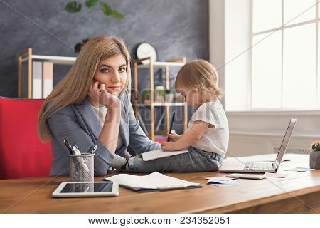 Tired Beautiful Business Mom Working On Laptop And Taking Notes While Spending Time With Her Cute Ba