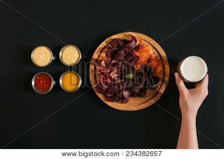 Cropped Shot Of Person Holding Glass Of Beer And Delicious Sliced Assorted Meat On Wooden Board With