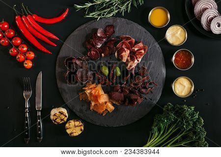 Top View Of Gourmet Assorted Meat On Slate Board, Various Sauces And Vegetables On Black
