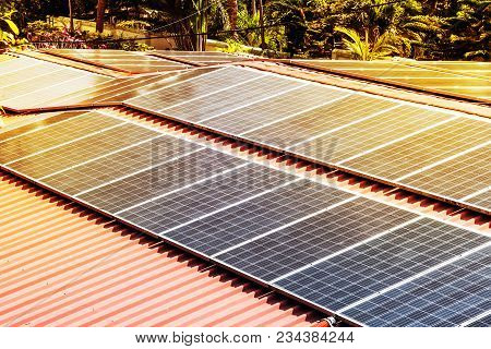 Roof With Solar Panels Fragment Under Sunny Blue Sky. Sun Is Shining On Black Solar Panels. Alternat