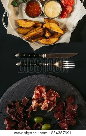 Top View Of Delicious Assorted Meat On Slate Board And Roasted Potatoes On Baking Paper With Fork An