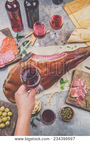 Mans Hand Holding Wine Glass Frome Above Table With Spanit Or Italian Appetizers, Whole Leg Of Ham S