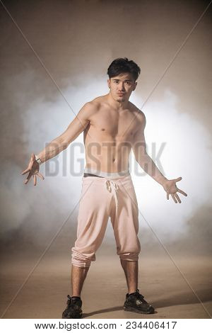 Self-confident And Charming Sportsmen Nacked To The Waist In White Pants On Foggy Street. Strong Han
