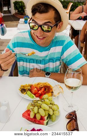 Happy Young Man Eating Food In Hotel. All Inclusive Concept. Summer Vacation. Having Lunch With Glas