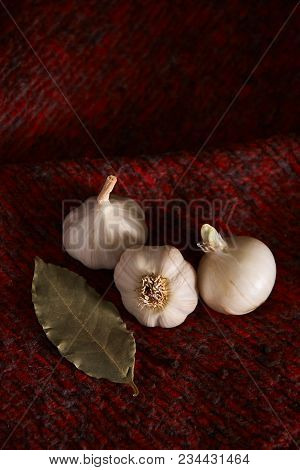 Garlic, Black Pepper And Bay Leaf On Dark Red Textile
