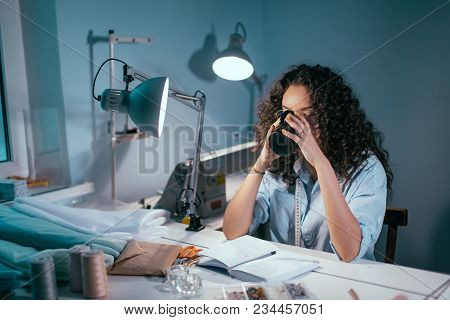 Nice Woman In Glasses With Curlu Hair Drinking Tea At The Table In Atelier. Having Break. A Sip Of W