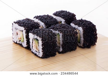 One Set Of California Rolls Covered Black Tobiko Or Masago Caviar On A Wooden Board On A White Backg
