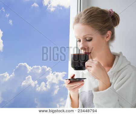 jonge mooie vrouw koffie drinken door het venster