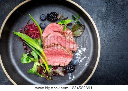 Traditional barbecue aged sliced fillet steak with wild garlic and fruits top view on a plate with copy space 