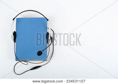 Audiobook On White Background. Headphones Put Over Blue Hardback Book, Empty Cover, Copy Space For A