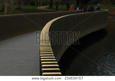The Brass Railing Of The Bridge Is Designed To Bend Across The Lake.