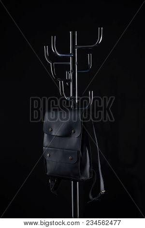 Black Leather Backpack Hanging On Coat Rack Isolated On Black