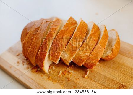 A Fresh Loaf Cut Into Pieces Lies On A Wooden Board, Next To A Knife-file For Bread. The Crust Crumb