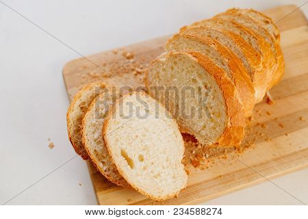 A Fresh Loaf Cut Into Pieces Lies On A Wooden Board, Next To A Knife-file For Bread. The Crust Crumb