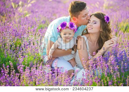 Mom, Dad And Their Little Daughter In A Beautiful Wreath Are Walking In A Lavender Field. Life In Pr