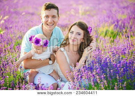 Mom, Dad And Their Little Daughter In A Beautiful Wreath Are Walking In A Lavender Field. Life In Pr