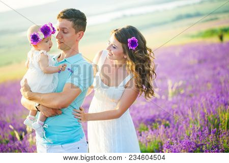 Mom, Dad And Their Little Daughter In A Beautiful Wreath Are Walking In A Lavender Field. Life In Pr