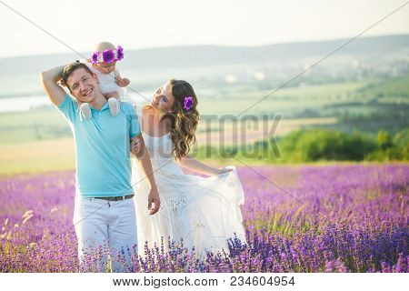Mom, Dad And Their Little Daughter In A Beautiful Wreath Are Walking In A Lavender Field. Life In Pr
