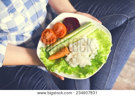 A Girl Holds A Plate With Rice And Vegetables. Healthy Eating Concept. Girl In Jeans And A Plaid Shi