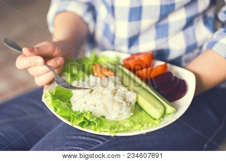 A Girl Holds A Plate With Rice And Vegetables. Healthy Eating Concept. Girl In Jeans And A Plaid Shi