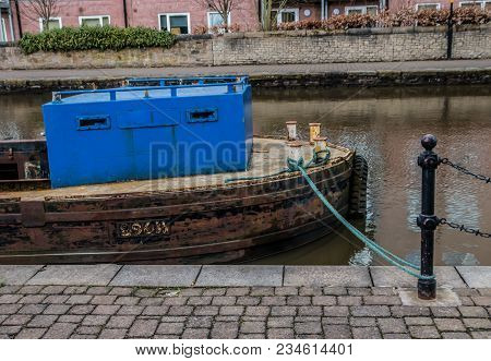 A Small Working Barge Is Moored Up Alongside The Paved Towpath