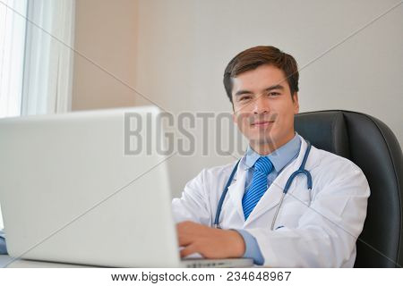 Smiling Doctor Posing In The Office, He Is Wearing A Stethoscope, Medical Staff On The Hospital Back