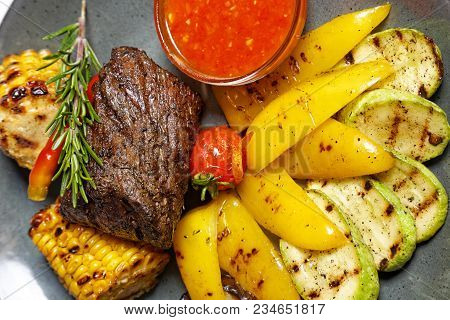 Fried Meat With Garnish Of Pepper, Zucchini, Tomato And Corn With Ajika Sauce Served On A Gray Plate