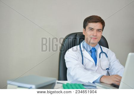 Smiling Doctor Posing In The Office, He Is Wearing A Stethoscope, Medical Staff On The Hospital Back