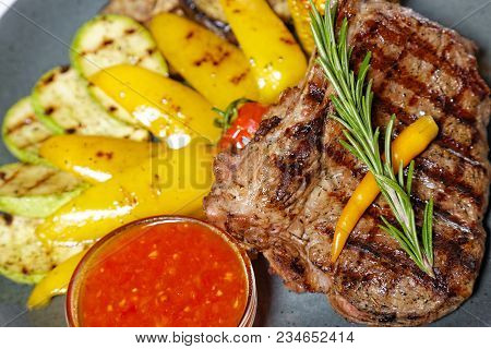 Fried Meat With Garnish Of Pepper, Zucchini, Tomato And Corn With Ajika Sauce Served On A Gray Plate