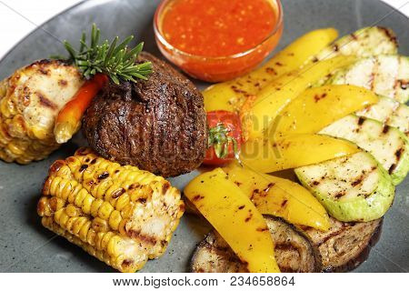 Fried Meat With Garnish Of Pepper, Zucchini, Tomato And Corn With Ajika Sauce Served On A Gray Plate